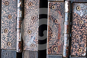 Close-up of two rusty metal door hinges on folding wooden doors.
