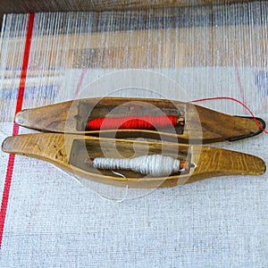 Close-up two shuttles and spools with red and white strings for the loom on a homespun textile