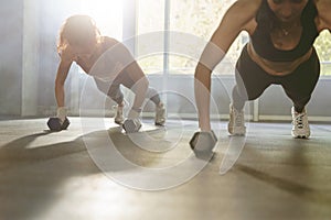 Close up of two sporty women doing push-up exercise with dumbbell. Strong females doing workout