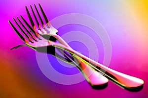 Close up of two stainless steel forks on abstract background with reflections