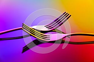 Close up of two stainless steel forks on abstract background with reflections