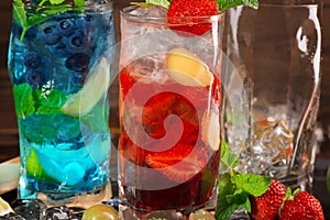 Close-up of two sweet bright cocktails with mint, lime, ice and berries as a background. Refreshing summer beverages for parties.