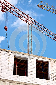Close-up of two tower cranes working against the backdrop of a new building and blue sky, selective focus