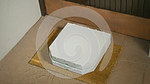 CLOSE UP: Two white pizza boxes sit on the brown doormat in front of closed door