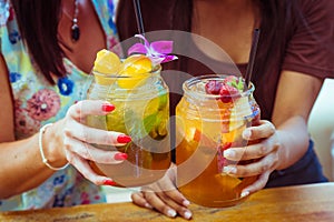 Close up of two women clink glasses with refreshing strawberry apple cocktail with lime and peach mint cold coctail