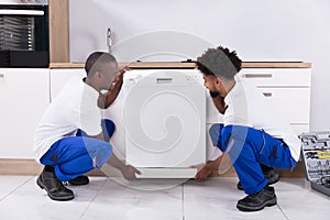 Two Handy Men Fixing The Dishwasher In The Kitchen