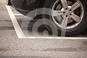 Close up of tyres car wheel from car parking inside white stipes at parking lot on asphalt