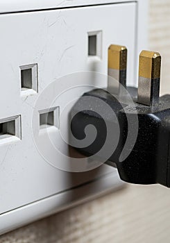 Close-up of a UK electrical outlet with a plug inserted. The socket is white with three