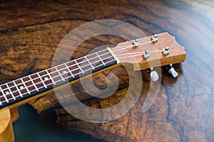 Close-up of a ukulele fretboard - small light brown instrument on beautiful wooden table