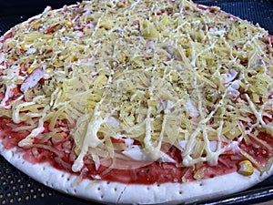 Close up of uncooked pizza prepared with cheese, corn, and crab stick for oven