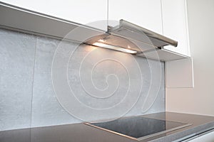 A close-up on under cabinet range hood, exhaust vent hood with lights working and modern electric stove, cooktop in gray and white