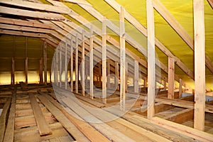 A close-up on an unfinished attic construction with wooden roof beams, planks, rafters, ceiling joists and vapor barrier film