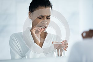 Close up unhappy African American woman taking pill, feeling unhealthy
