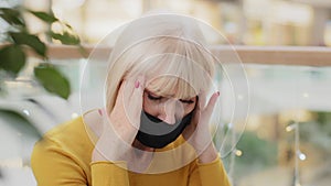 Close-up unhappy caucasian middle-aged woman in medical mask sitting indoors holding hands behind head suffering