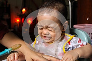 Close up of unhappy little seven months old son in see through plastic bib screaming and crying in chair for babies after mom made