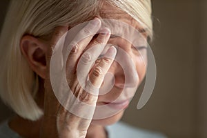 Close up unhappy mature woman crying, touching forehead, feeling unwell