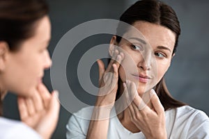 Close up unhappy woman looking at acne spots in mirror