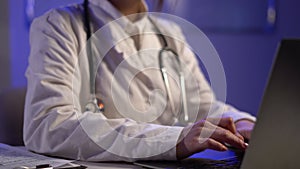 Close up of unknown female doctor sitting at the table in hospital and typing at laptop computer.