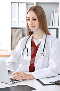 Close-up of unknown female doctor typing on laptop computer while sitting at the table