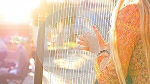 CLOSE UP Unknown street musician gently plucking the strings of a harp at sunset