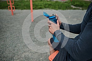 Close-up of an unrecognizable athlete holding a fresh water bottle rehydrating his body after exercise, bodybuilding and outdoor