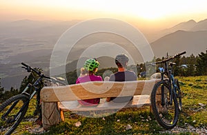 CLOSE UP: Unrecognizable bicycle riders sit and observe the sunset from a bench