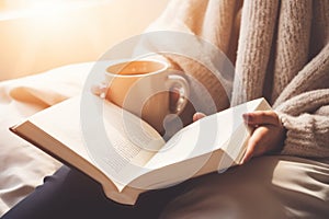 Close up unrecognizable girl woman reading book in cozy bed bedroom with warm coffee cup tea cocoa mug relaxation