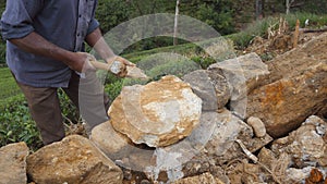 Close up of unrecognizable indian man cutting a block of granite with hammer in botanical garden. Adult human hitting