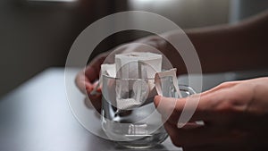 Close-up of unrecognizable man opening and putting bag of drip coffee in glass cup at table in kitchen room. Preparing