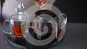 Close-up. An unrecognizable pregnant woman pours hot, freshly brewed tea into a glass cup from a glass infuser and adds