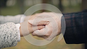 Close-up of unrecognizable senior man and woman holding hands outdoors. Old Caucasian husband and wife dating in spring