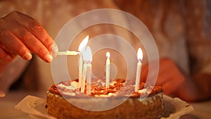 Close-up. An unrecognizable woman lights candles on a birthday cake while sitting at the table.