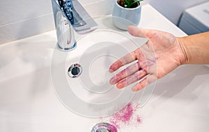 Close up of unrecognizable woman removing purple glitter of her hand into washbasin at bathroom