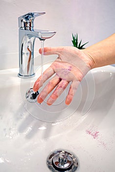 Close up of unrecognizable woman washing purple glitter of her hand into a washbasin at bathroom