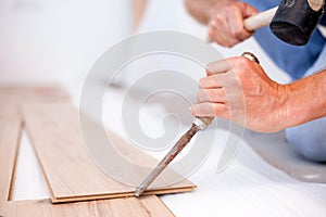 Close-up of unrecognizable young man chiseling grooves on a laminate floor tile, installing laminate flooring