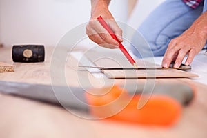 Close-up of unrecognizable young man measuring and marking laminate floor tile for cutting, installing laminate flooring