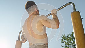 CLOSE UP: Unrecognizable young sportsman doing pull ups in the sunny nature.