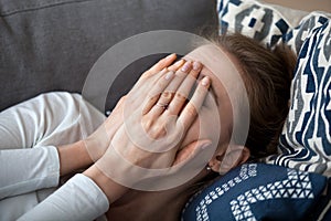 Close up upset frustrated woman covering face with hands, lying on sofa