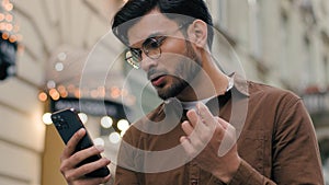 Close up upset unhappy Indian Arabian ethnic man young guy businessman male using looking mobile phone bad connection