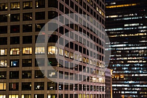 Close up urban scene of modern buildings at night with colorful glowing windows, lights and reflections