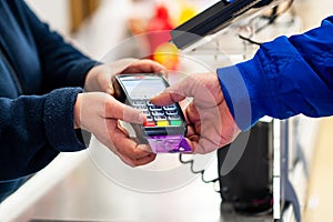 Close up of using credit card pos terminal to pay. Hands entering the password of creditcard for payment.