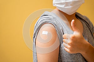 Close up of Vaccinated asian teen girl in face mask showing plaster bandage on her arm after getting covid-19 vaccine injection on