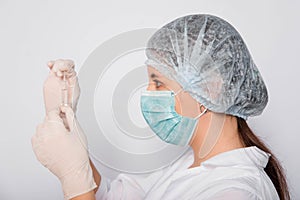 Close-up of a vaccine ampoule in the hands of a woman doctor. Lab technician in a white coat, medical hat, mask and gloves, holds