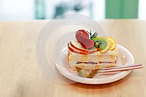 Close Up Vanilla Cake with fruits on top, strawberry, kiwi, orange, apple and cherry, in the white plate on the wooden table