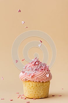 Close-up of vanilla cupcake with pink whipped butter cream top. Cream cheese frosting on muffin decorated with little pink heart