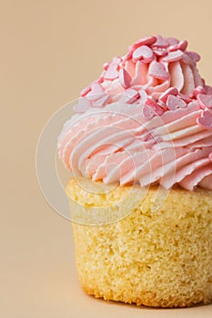 Close-up of vanilla cupcake with pink whipped butter cream top. Cream cheese frosting on muffin decorated with little pink heart