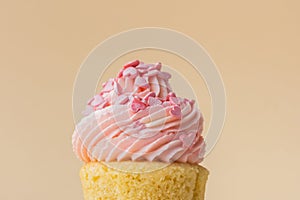 Close-up of vanilla cupcake with pink whipped butter cream top. Cream cheese frosting on muffin decorated with little pink heart