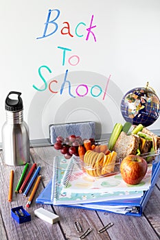 Close up of various school supplies and a lunch kit against a whiteboard. Back to school concept.
