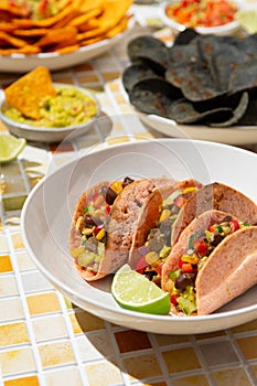 close up vegetarian tacos with vegetable salsa and beans with lime on a plate on a colorful tile. Mexican food, nachos