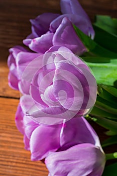 Close-up vertical photo of a bouquet of tulips with lilac petals lies on a wooden table